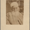 Photograph of man with beard in brimless hat and cloak, seated and facing camera