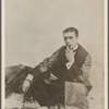 Publicity photograph of William Gillette in role of Sherlock Holmes, sitting cross-legged on fur rug, smoking a pipe