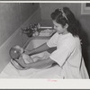NYA (National Youth Administration) girl who lives at the resident center at the FSA (Farm Security Administration) farm workers' community at Eleven Mile Corner learns to bathe a baby