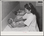 NYA (National Youth Administration) girl who lives at the resident center at the FSA (Farm Security Administration) farm workers' community at Eleven Mile Corner learns to bathe a baby