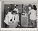Eleven Mile Corner, AZ. FSA farm workers' community. Girls, who live at the NYA resident center learning baby care. The nurse, who divides her time between working at the hospital and instructing the NYA girls, is showing them how to care for a well baby