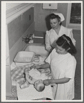 Eleven Mile Corner, AZ. FSA farm workers' community. Girls, who live at the NYA resident center learning baby care. The nurse, who divides her time between working at the hospital and instructing the NYA girls, is showing them how to care for a well baby