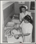 Eleven Mile Corner, AZ. FSA farm workers' community. Girls, who live at the NYA resident center learning baby care. The nurse, who divides her time between working at the hospital and instructing the NYA girls, is showing them how to care for a well baby