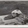 Migrant boy playing the guitar on pallet while camped near Prague, Oklahoma. Lincoln County, Oklahoma