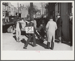 Tobacco auctioneer who "bet on Carolina" and lost, pays off the wager by pushing the warehouseman in a wheelbarrow from the warehouse to the courthouse. Durham, North Carolina