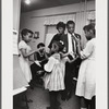 Baldwin standing in kitchen with extended family, with two pairs of girls playing hand-clapping games