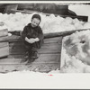 Young daughter of Frank H. Shurtleff sitting outside sugar house where sap from maple trees is boiled down into maple syrup. The Shurtleff farm has about 400 acres and was