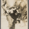 Photograph of woman walking with book and gloves in hand, man in hat in the background