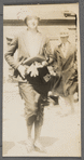 Photograph of woman walking with book and gloves in hand, man in hat in the background