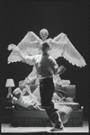 Ellen McLaughlin and Stephen Spinella, with a figure crossing downstage, in Angels in America: Millennium Approaches