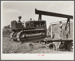 Loading repaired tractor from bank to truck ready to leave FSA (Farm Security Administration) warehouse depot in Atlanta, Georgia