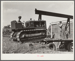 Loading repaired tractor from bank to truck ready to leave FSA (Farm Security Administration) warehouse depot in Atlanta, Georgia