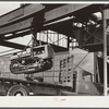 Tractor, transported by truck to FSA (Farm Security Administration) warehouse depot for repairs, being hoisted by Shepard crane to shop inside. Atlanta, Georgia