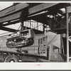 Tractor, transported by truck to FSA (Farm Security Administration) warehouse depot for repairs, being hoisted by Shepard crane to shop inside. Atlanta, Georgia