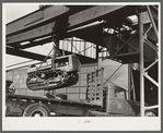 Tractor, transported by truck to FSA (Farm Security Administration) warehouse depot for repairs, being hoisted by Shepard crane to shop inside. Atlanta, Georgia