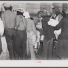 Black day laborers brought in truck from nearby towns, waiting to be paid off for cotton picking and buy supplies inside plantation store on Friday night. Marcella Plantation. Mississippi Delta. Mississippi
