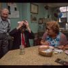 Man in red tie (with toupee?) and woman in blue apron (laughing) seated at table, Retired Owners and Workers