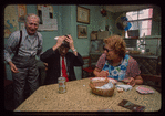 Man in red tie (with toupee?) and woman in blue apron (laughing) seated at table, Retired Owners and Workers