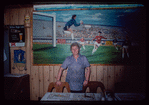 Restaurant worker in blue shirt in front of painting, Nea Hellas