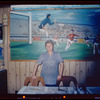 Restaurant worker in blue shirt in front of painting, Nea Hellas