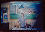 Restaurant worker in blue shirt in front of painting, Nea Hellas