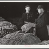 Tobacco warehouseman examining farmer's tobacco before auction sale. Durham, North Carolina