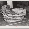 Worker in tobacco warehouse resting on top of empty tobacco baskets after auction sale. Durham, North Carolina