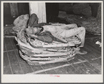 Worker in tobacco warehouse resting on top of empty tobacco baskets after auction sale. Durham, North Carolina