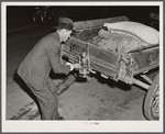 Mr. Elvin Wilkins fastening a new lantern on the back of his trailer in which he brought his tobacco to the warehouse for auction sale. He is returning home with a bag of hog feed in the trailer. Durham, North Carolina