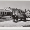 Lloyd Young, FSA (Farm Security Administration) client, hauling load of hay past the office and Community building of Plum Bayou Project, Arkansas (see general caption)
