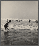 Beach scene with crowd of people catching waves in the ocean