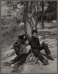 Three young children seated around the base of a tree