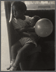 Young girl holds a toddler in her lap, and a balloon in hand 