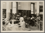 Patrons in reading room; two girls in hats in foreground