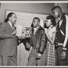 Langston Hughes with young library visitors at Schomburg Collection, holding a copy of his new book 