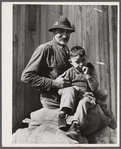 Spanish muskrat trapper and his grandson sitting on sacks of dried muskrat pelts, in front of their camp in the marshes. Delacroix Island, Saint Bernard Parish, Louisiana.