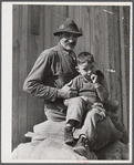 Spanish muskrat trapper and his grandson sitting on sacks of dried muskrat pelts, in front of their camp in the marshes. Delacroix Island, Saint Bernard Parish, Louisiana.