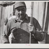 Spanish muskrat trapper by his marsh camp with reeds in his hand. These reeds are used to mark location of traps. Delacroix Island, Saint Bernard Parish, Louisiana.