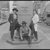 Publicity photograph of Edward James Olmos, Luis Valdez, and Daniel Valdez posing in Times Square before the base of a George M. Cohan commemorative statue ("Give my Regards to Broadway") during the stage production Zoot Suit