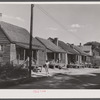 A street in the Negro quarter of Elizabeth City, North Carolina, where many of the migrants find lodging. In the background is one of the trucks that take them to and from work.