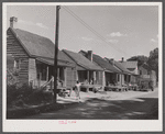 A street in the Negro quarter of Elizabeth City, North Carolina, where many of the migrants find lodging. In the background is one of the trucks that take them to and from work.