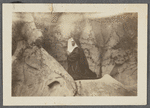 Nun kneeling amid rock formation, undated