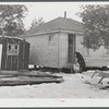 Mrs. Carol Porter setting out milk bottle. Shot shows small shack the Porters lived in while they were building their house.