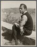 James Baldwin sitting on low wall by lake