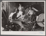 Fishermen in repair shack repairing nets and sharpening tools. The twine of these nets is impregnated with coal tar;
