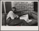 Negro reading in front of his alley dwelling home, Washington, D.C.