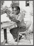 James Baldwin in eyeglasses and checkered shirt marking pages