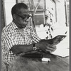 James Baldwin in eyeglasses and checkered shirt marking pages