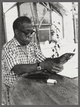 James Baldwin in eyeglasses and checkered shirt marking pages