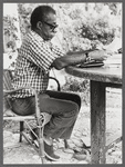 James Baldwin in eyeglasses and checkered shirt marking pages